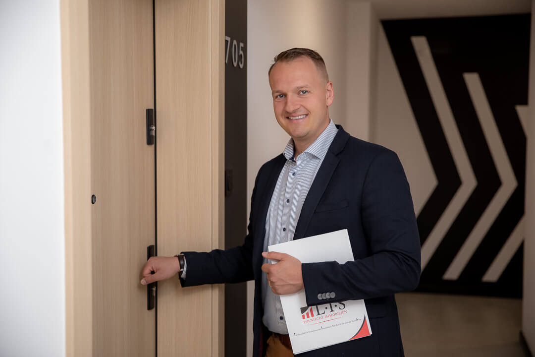 David Lis vor der Wohnungstür mit dem Exposé einer Immobilie in Polen